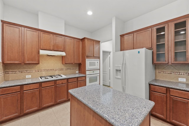 kitchen with under cabinet range hood, brown cabinets, white appliances, and glass insert cabinets