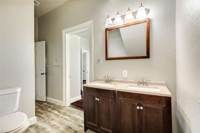 bathroom featuring double vanity, toilet, wood finished floors, and a sink
