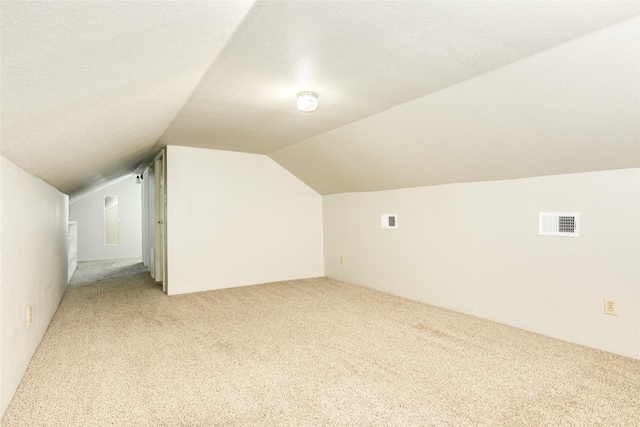 bonus room with lofted ceiling, light colored carpet, visible vents, and a textured ceiling