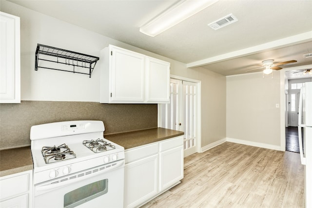 kitchen featuring visible vents, white range with gas cooktop, light wood-style flooring, dark countertops, and white cabinetry