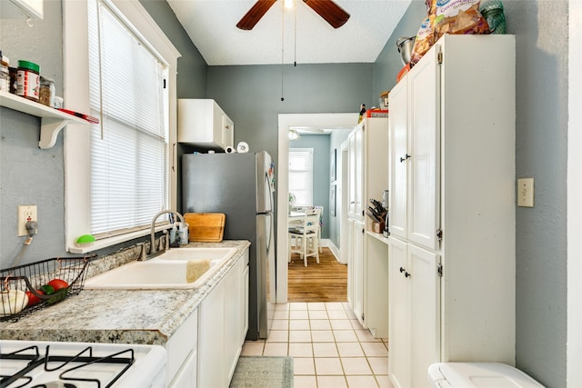 kitchen with light tile patterned flooring, ceiling fan, a sink, light countertops, and white cabinets