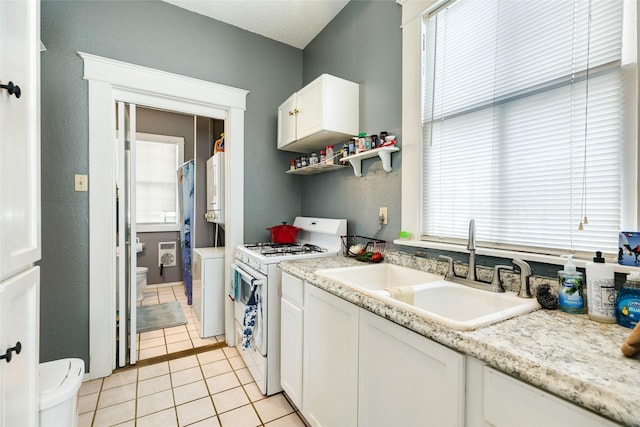 kitchen with light countertops, white gas range, light tile patterned floors, white cabinetry, and a sink