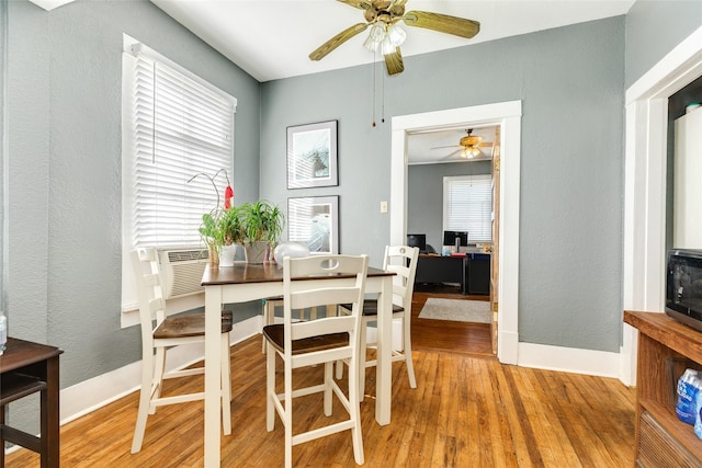 dining room featuring a textured wall, baseboards, light wood-style floors, and a ceiling fan