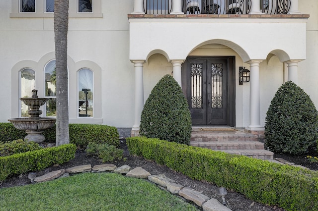 view of exterior entry with french doors, a balcony, and stucco siding