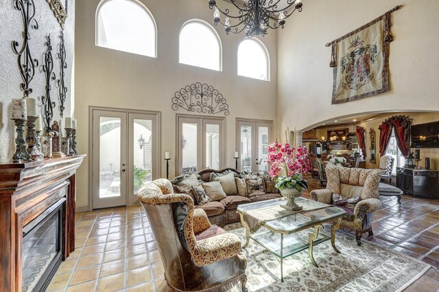 living room with a glass covered fireplace, a notable chandelier, french doors, and arched walkways