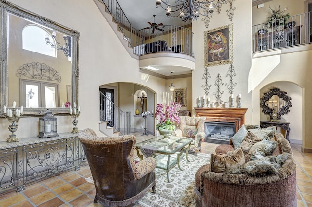 living area featuring arched walkways, a high ceiling, a glass covered fireplace, and stairs