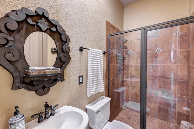 bathroom with a sink, toilet, a stall shower, and a textured wall