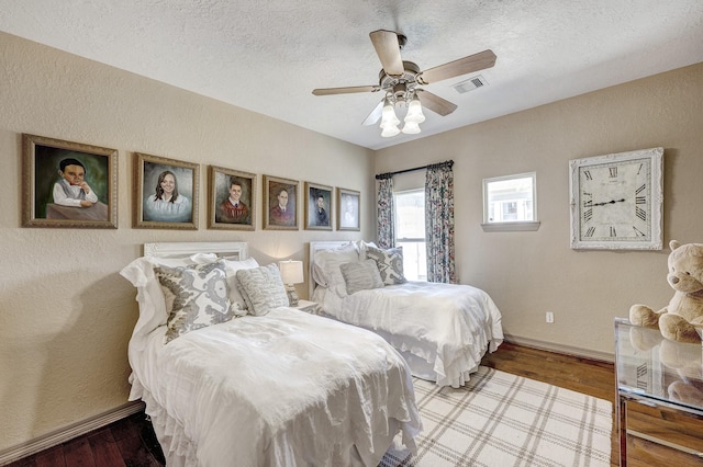 bedroom with a textured ceiling, wood finished floors, visible vents, and baseboards