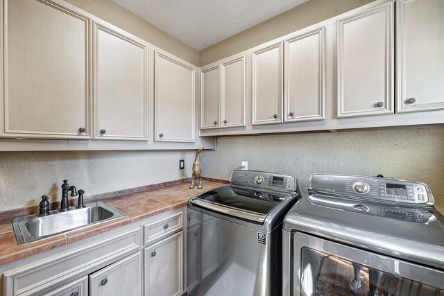 washroom with cabinet space, washing machine and dryer, a textured wall, and a sink