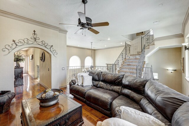 living room with a ceiling fan, wood finished floors, baseboards, arched walkways, and crown molding