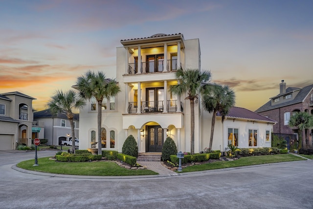 mediterranean / spanish-style house with french doors, a balcony, driveway, and stucco siding