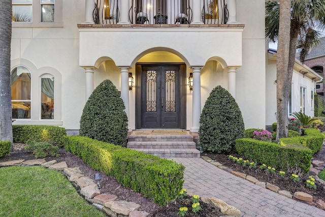 entrance to property with stucco siding, french doors, and a balcony