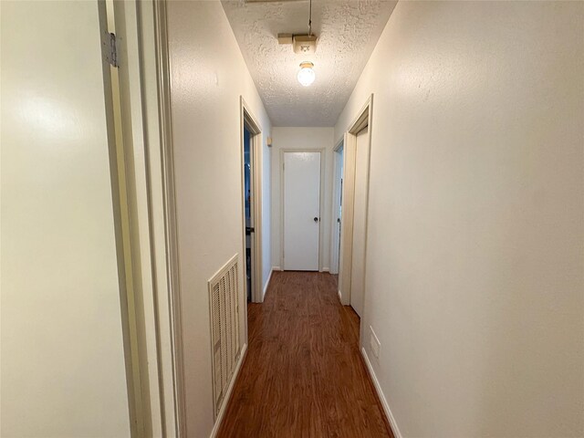 hall featuring visible vents, a textured ceiling, baseboards, and wood finished floors