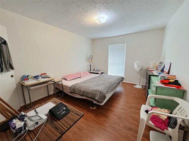 bedroom featuring a textured ceiling, baseboards, and wood finished floors