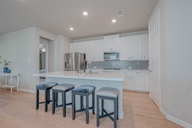 kitchen featuring backsplash, stainless steel appliances, a kitchen bar, and a kitchen island with sink