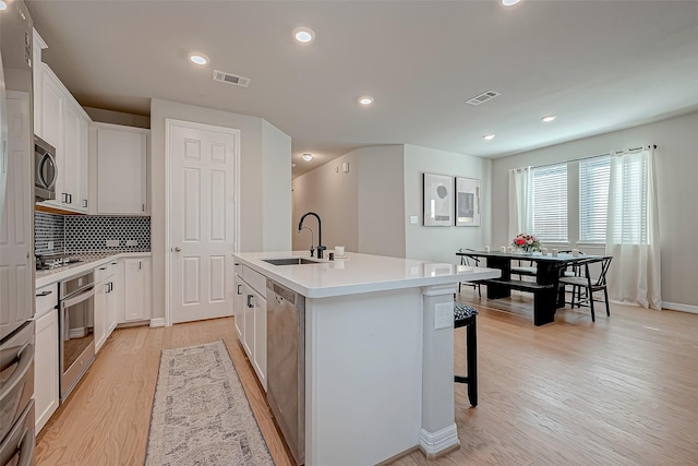 kitchen with visible vents, light wood-type flooring, an island with sink, stainless steel appliances, and a sink