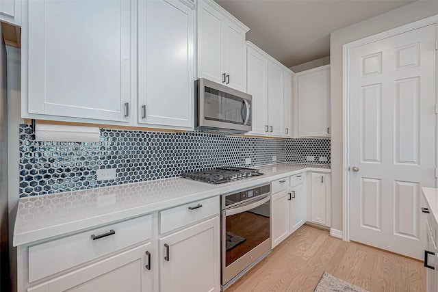 kitchen featuring light wood-style flooring, tasteful backsplash, stainless steel appliances, white cabinets, and light countertops