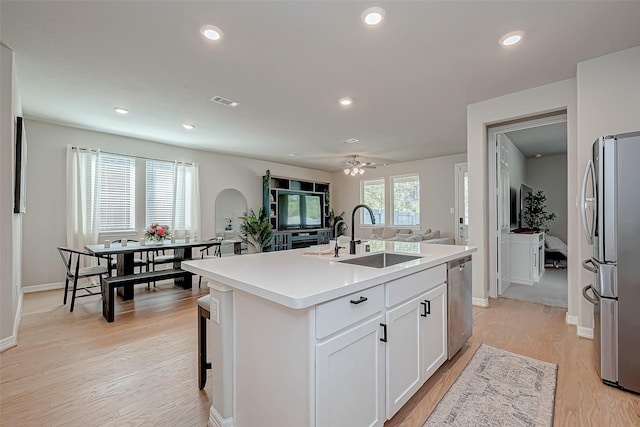 kitchen featuring light wood finished floors, an island with sink, a sink, appliances with stainless steel finishes, and a wealth of natural light