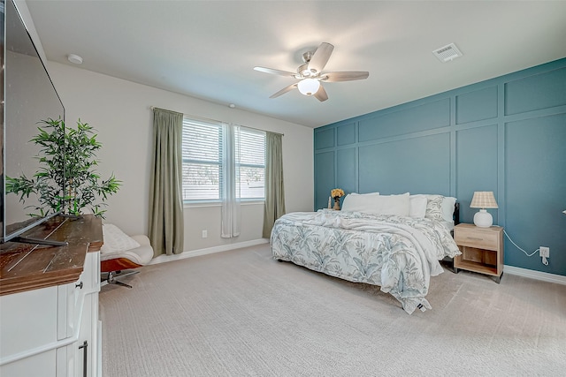 bedroom featuring a decorative wall, a ceiling fan, visible vents, and light carpet