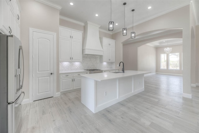 kitchen with a notable chandelier, stainless steel refrigerator with ice dispenser, custom range hood, a sink, and arched walkways