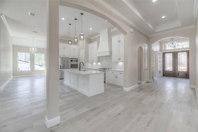 kitchen featuring arched walkways, custom range hood, light wood-style floors, french doors, and a chandelier