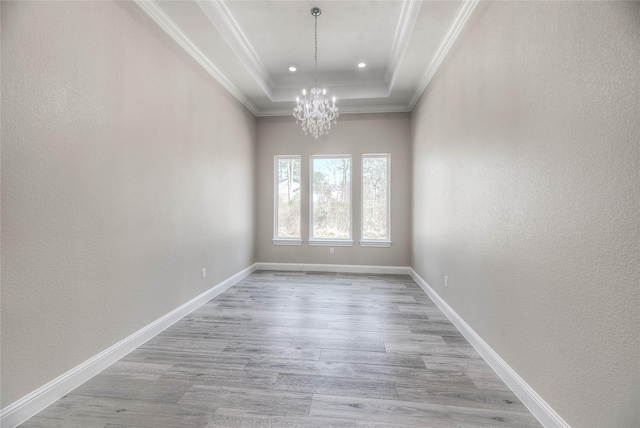 empty room featuring crown molding, baseboards, a chandelier, wood finished floors, and a raised ceiling