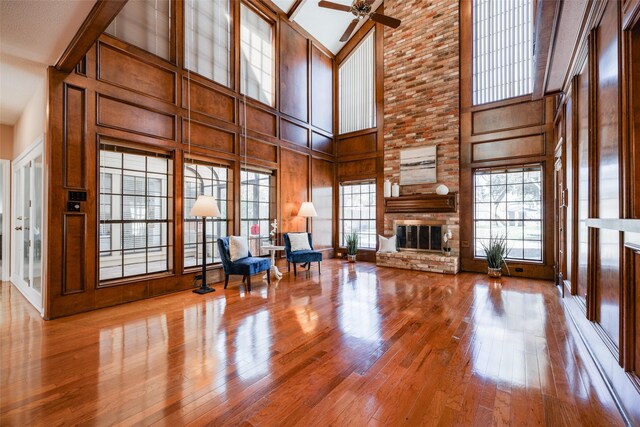 unfurnished living room featuring wood walls, a brick fireplace, a ceiling fan, and wood-type flooring