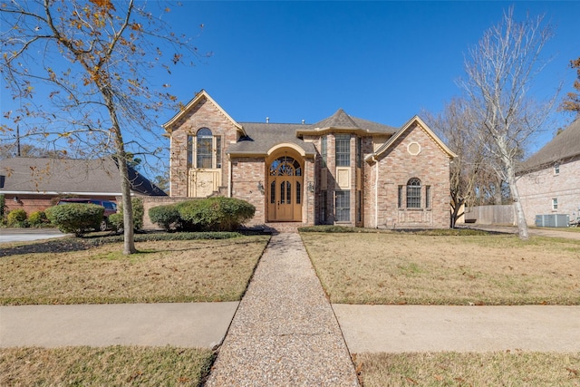 french country home featuring brick siding, a front lawn, and central AC