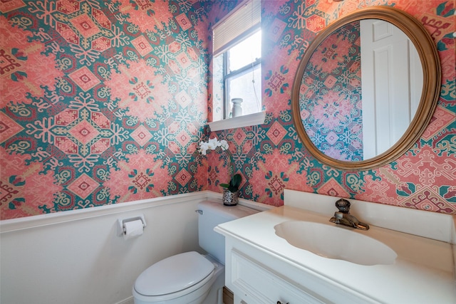 half bath with wallpapered walls, toilet, and vanity