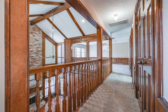 hall with visible vents, a textured ceiling, carpet, wainscoting, and vaulted ceiling with beams