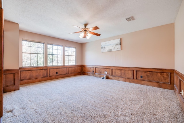 spare room featuring carpet flooring, visible vents, a wainscoted wall, and a textured ceiling