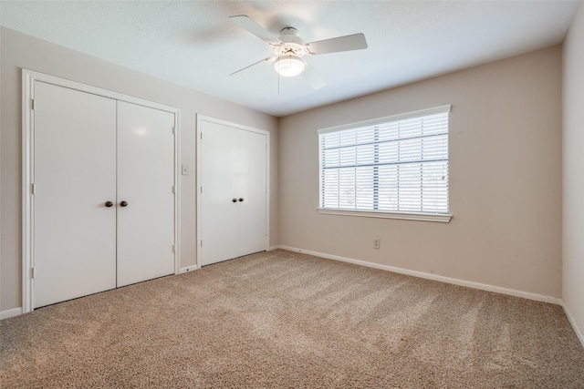 unfurnished bedroom featuring two closets, a textured ceiling, carpet floors, baseboards, and ceiling fan