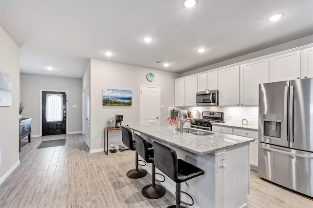 kitchen featuring light wood finished floors, appliances with stainless steel finishes, an island with sink, and a sink