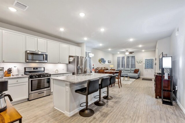 kitchen featuring visible vents, stainless steel appliances, decorative backsplash, white cabinets, and open floor plan