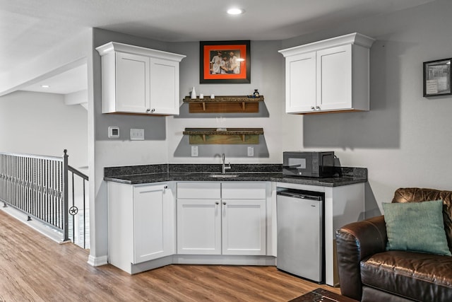 kitchen with black microwave, light wood-style floors, white cabinets, fridge, and a sink