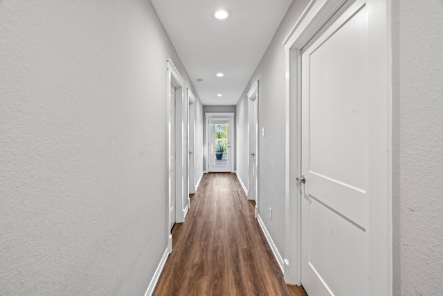 corridor with dark wood finished floors, recessed lighting, baseboards, and a textured wall