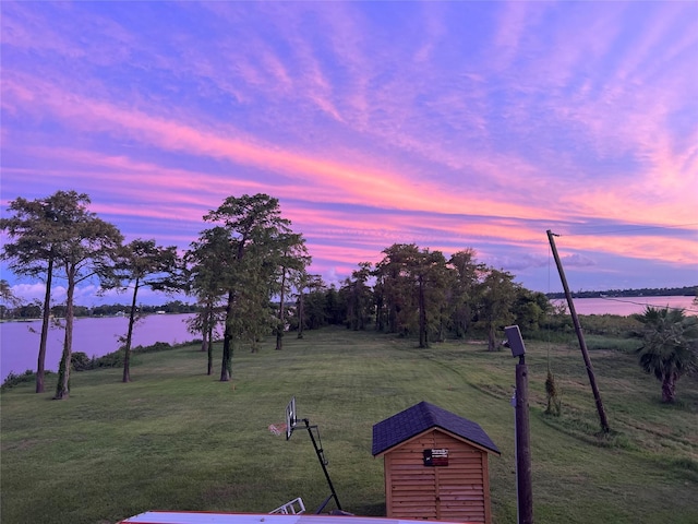 yard at dusk featuring an outdoor structure and a water view