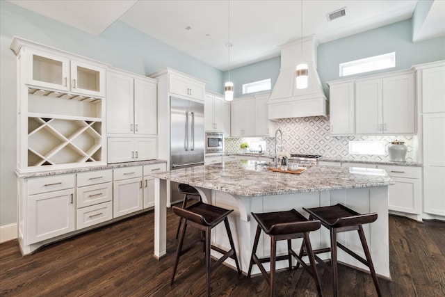 kitchen featuring premium range hood, visible vents, a kitchen bar, white cabinetry, and built in appliances