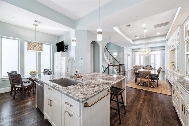 kitchen with arched walkways, visible vents, a raised ceiling, and a sink