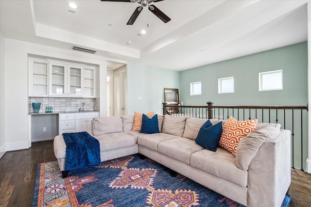 living room featuring visible vents, a ceiling fan, dark wood-style flooring, and a tray ceiling