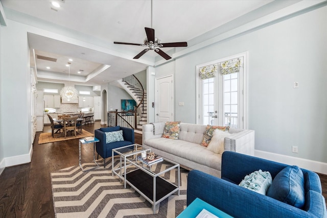 living room featuring visible vents, stairway, dark wood-style floors, arched walkways, and a raised ceiling