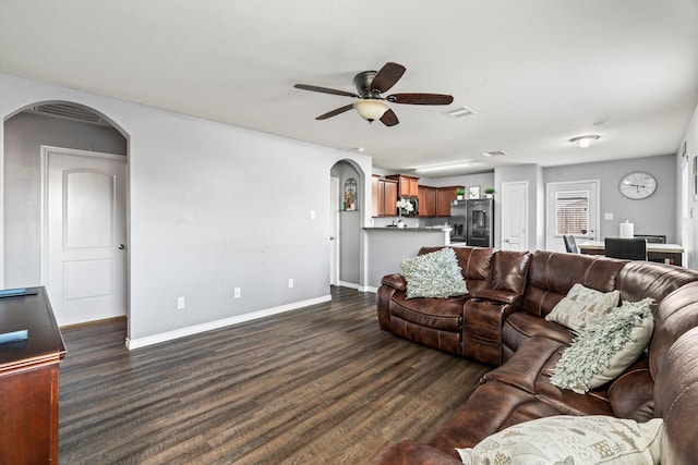 living area featuring visible vents, a ceiling fan, dark wood finished floors, arched walkways, and baseboards