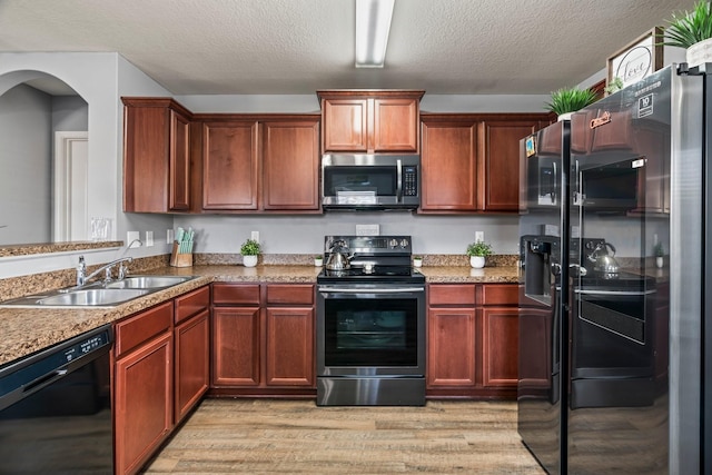 kitchen featuring arched walkways, a sink, light wood-style floors, appliances with stainless steel finishes, and a textured ceiling