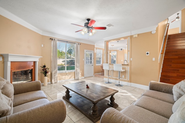 living room with visible vents, ornamental molding, a ceiling fan, baseboards, and stairs