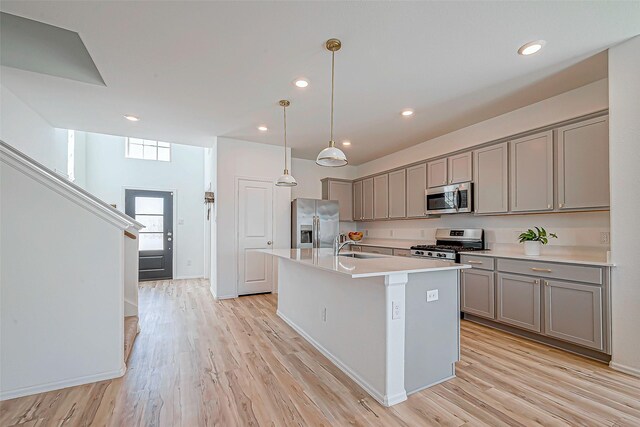 kitchen with a center island with sink, light wood-style flooring, gray cabinets, stainless steel appliances, and light countertops