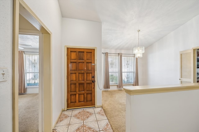 foyer entrance featuring a chandelier, light colored carpet, light tile patterned flooring, and vaulted ceiling