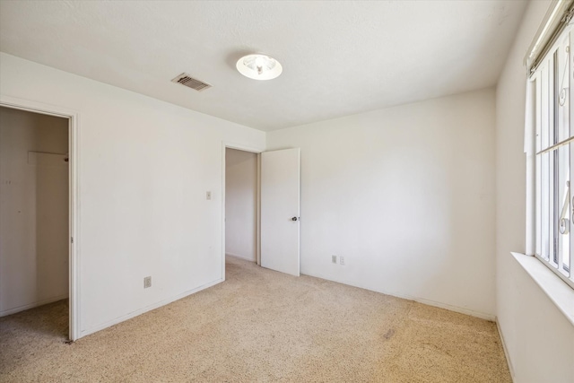 unfurnished bedroom featuring a spacious closet, light colored carpet, and visible vents