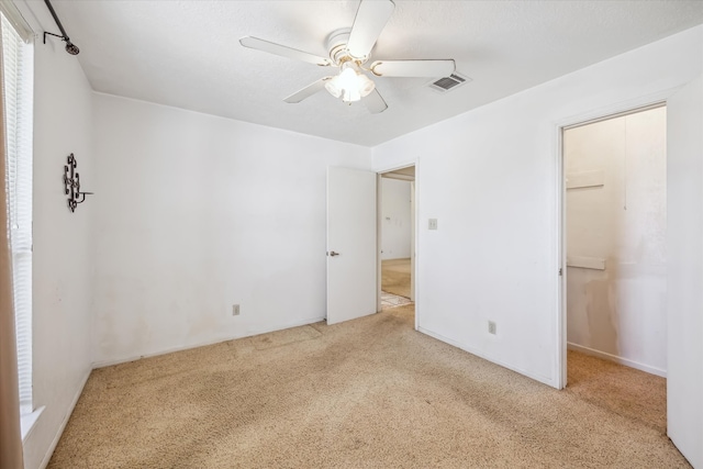 unfurnished bedroom with a ceiling fan, visible vents, a closet, a walk in closet, and carpet flooring