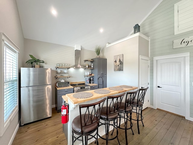 kitchen featuring range hood, stainless steel appliances, lofted ceiling, and wood-type flooring