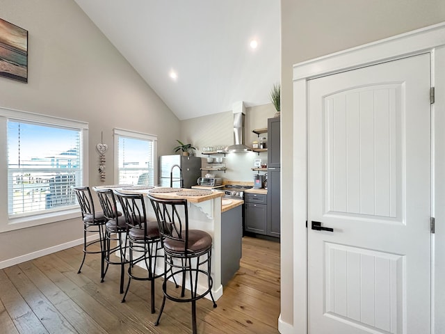 kitchen with gray cabinetry, light wood-style flooring, a kitchen breakfast bar, freestanding refrigerator, and wall chimney exhaust hood